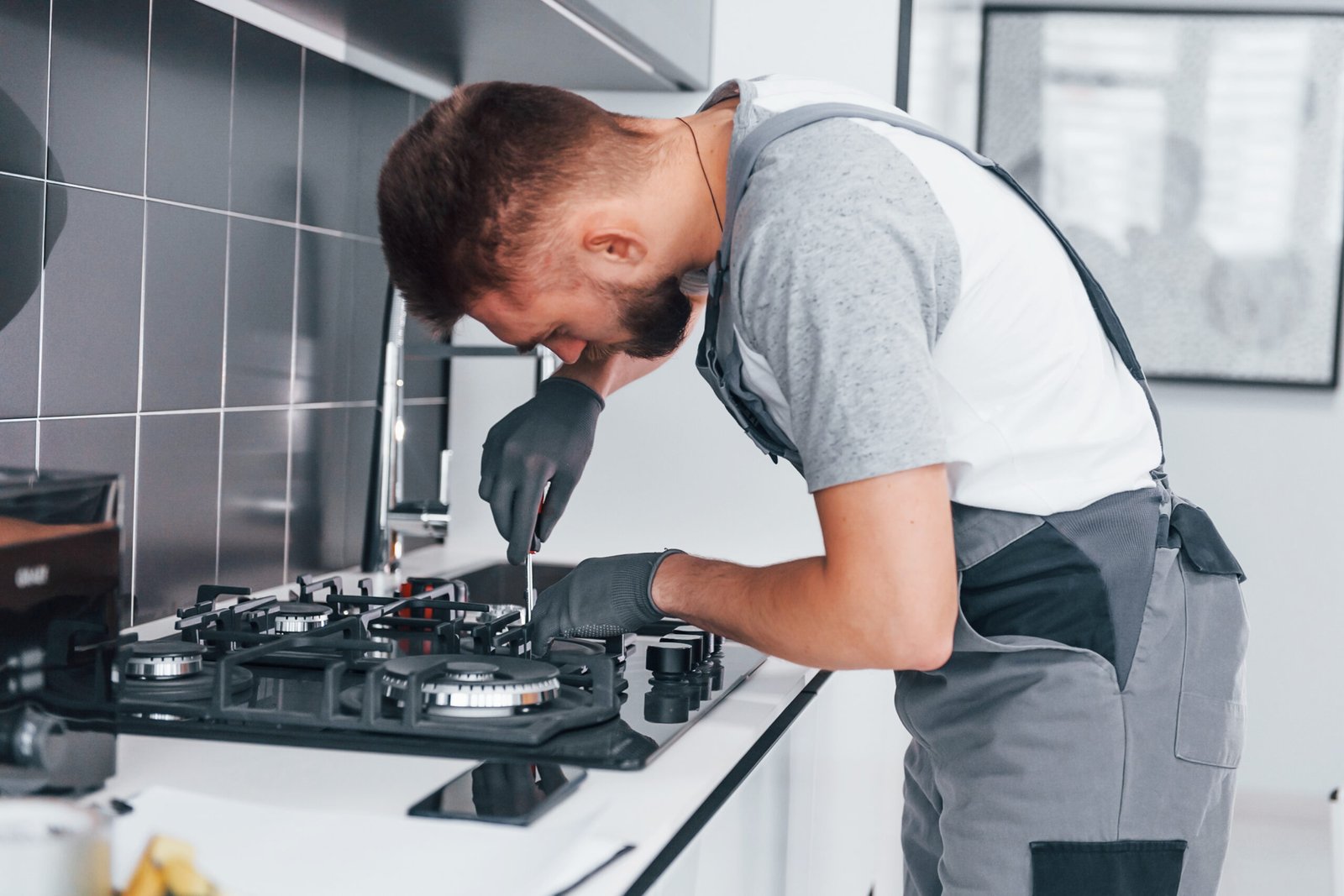 Young professional plumber in grey uniform working on the kitchen.